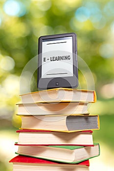 E-learning and reading. E-book reader is at the top of the stack of books. The Park is blurred in the background. Concept of