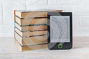 E-reader near stack of paper books on a white wooden table. Copy space on e-book display. E-reading on anti-glare screen for