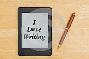 An e-reader on a wood desk with a pen with text I love writing