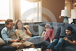 They each prefer their own entertainment. a couple watching tv while their kids are busy using digital tablets at home.