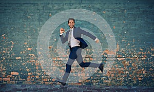 Eager to succeed. Portrait of a young corporate businessman jumping midair against a brick wall.