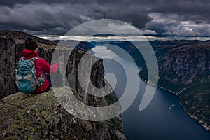Eagle head viewpoint near Kjeragbolten Lysebotn Norway Young woman sits by the edge of the lysefjorden