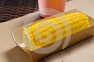 An ear of boiled corn in an eco-friendly cardboard box next to a milkshake