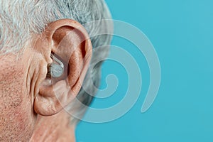 Ear of an elderly person with hearing aid on blue background