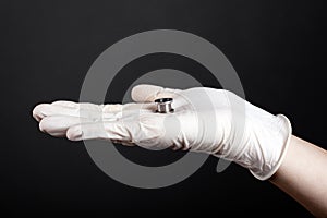 Ear jewelry, hand in a white disposable glove holds in his palm a tunnel for the ear of silver color on a dark background close-up