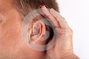 Ear of a man wearing hearing aid and cupping his hand behind his