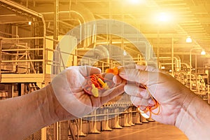 Ear plugs hearing protection in men& x27;s hand on factory worker background,safety concept