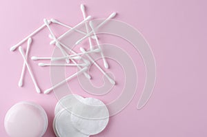 Ear sticks and cotton pads on pastel pink background. Makeup removal and skin care concept.