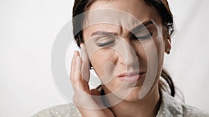 Earache. Suffering woman on white background with emotions of pain on her face touches her ear. Close-up
