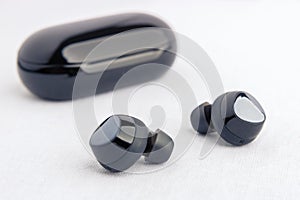 Earbud headphones side profile - displayed in front of opened black wireless earbud charging case