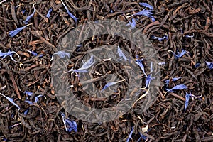 Earl grey with corn flower petals, black dry tea leaves background