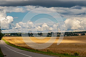early autumn landscape: road, harvested field, clouds