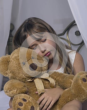 Early awakening. Alarm clock standing on bedside table. Wake up of an asleep young girl holding teddy bear in bed on a
