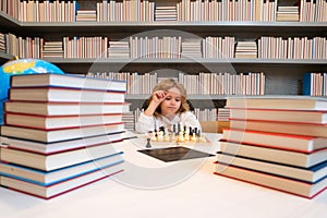 Early development. Smart boy play chess in the library by the bookshelves with many books. Educational concept. Boy