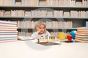 Early development. Smart child play chess in the library by the bookshelves with many books. Educational concept. Boy