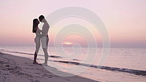 early in the morning at dawn or in the evening at sunset a young couple in love, a man and a woman, stand on the ocean