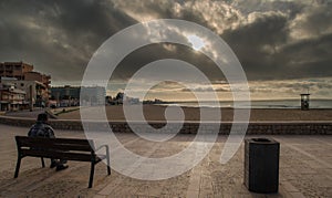 Early morning on the embankment of the Mediterranean Sea man admires the dawn sitting on a bench