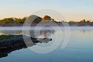 Early morning fog on lake with fall colors in background