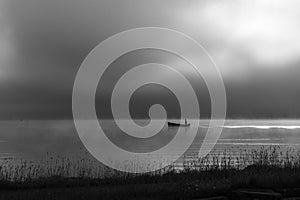 An early morning at Lac de Joux, Switzerland: A lone fisherman on a boat, fog is still hiding the rising sun