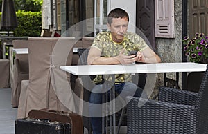 Early morning lonely tired Serious hipster tourist man holding mobile phone in cozy cafe interior