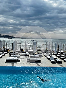 Early morning at luxury hotel by the sea. Lonely woman swims in azure water of pool