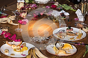 Early morning after the party. Glasses and plates on the table with confetti and serpentine, leftovers, flower petals
