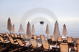 Early morning on sandy beach without people with empty chaise lounges, sun beds, sunshades, summer umbrella parasol, loungers.