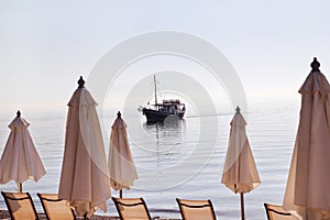 Early morning on sandy beach without people with empty chaise lounges, sun beds, sunshades, summer umbrella parasol, loungers.