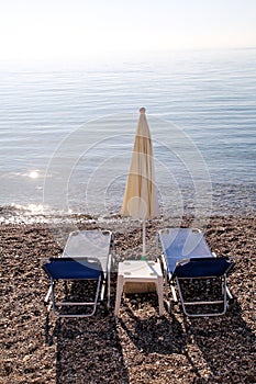 Early morning on sandy beach without people with empty chaise lounges, sun beds, sunshades, summer umbrella parasol, loungers.