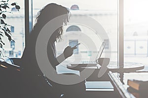 Early morning, silhouette of young woman with disheveled hair sitting at table in front of window