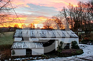 Early morning snowy barn with a vibrant orange sunrise behind it.