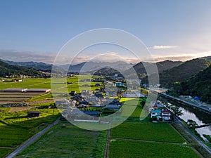 Early morning sun shines through mountains on small village and rice fields