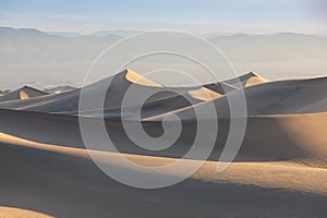 Early Morning Sunlight Over Sand Dunes And Mountains At Mesquite flat dunes, Death Valley National Park, California USA