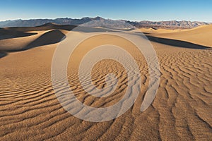 Early Morning Sunlight Over Sand Dunes And Mountains At Mesquite flat dunes, Death Valley National Park, California USA