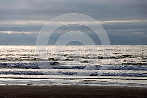 Early morning sunrise at sandy beach, where waves roll in under stormy skies