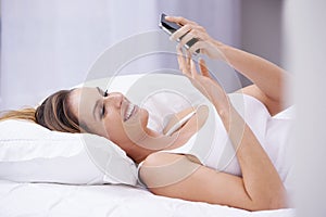 Early morning text messages...An attractive young woman reading a text message while lying in bed.