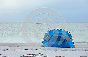 Early morning time camping on the beach in a tent with a sailboat in the distance