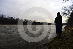 Early spring fisherman fishing off bank of fast flowing river at