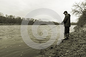 Early spring fisherman standing on the bank of a fast flowing ri