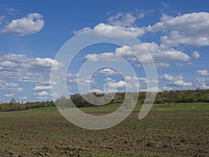 Early spring Prague landscape with brown field, green grass, trees with fresh lush leaves and blue sky, white fluffy clouds