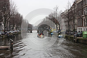 Early spring scene in Amsterdam city. Tours by boat on the famous Dutch canals. Cityscape with canal houses in Holland,