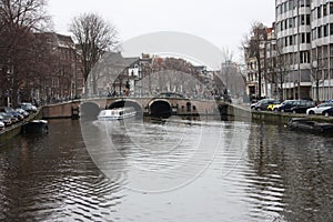 Early spring scene in Amsterdam city. Tours by boat on the famous Dutch canals. Cityscape with canal houses in Holland,