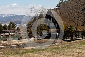 Early spring scenic landscape photograph of a traditional thatched roof house in rural Japan next to a rice paddy