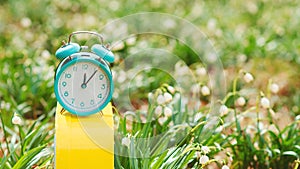 Early spring weather. Classic alarm clock with bells on nature background. Daylight saving time reminder