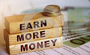 Earn More Money written on a wooden blocks, coins and bills. Business and career concept