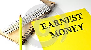 EARNEST MONEY text written on a yellow paper with notebook