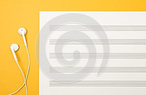 Earphones and blank music sheet on yellow background