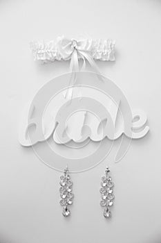 Earrings and garter of the bride with word bride lie on the white table, BW