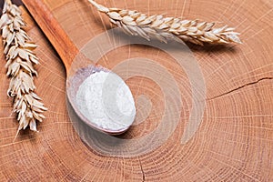 Ears of wheat and flour in the wooden spoon on the table