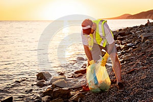 Earth Day. Volunteer man wearing vest in rubber gloves cleaning pebble wild beach. Copy space. Concept of ocean's